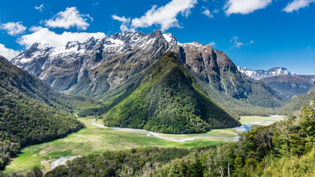 Panoramic view of the Humboldt Mountains in New Zealand, featuring lush green valleys, snow-capped peaks, and winding rivers under a vibrant blue sky.