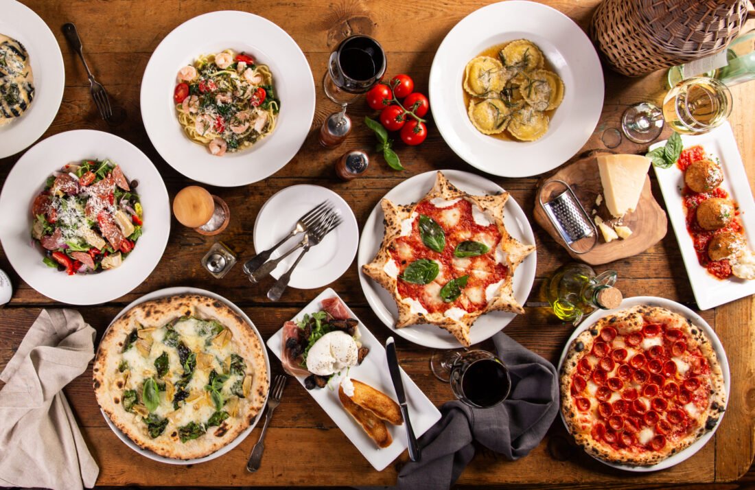 Big dinner table with italian food, pizzas and pastas, appetizers and wine