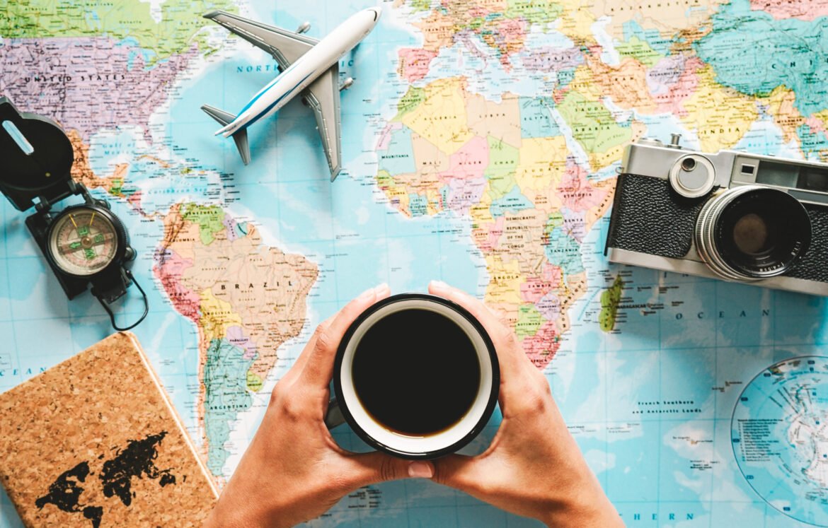 Top view of young woman planning her vacation using world map while drinking coffee - Tourist pointing the next travel destination - Concept of adventure, tourism, and traveling people lifestyle