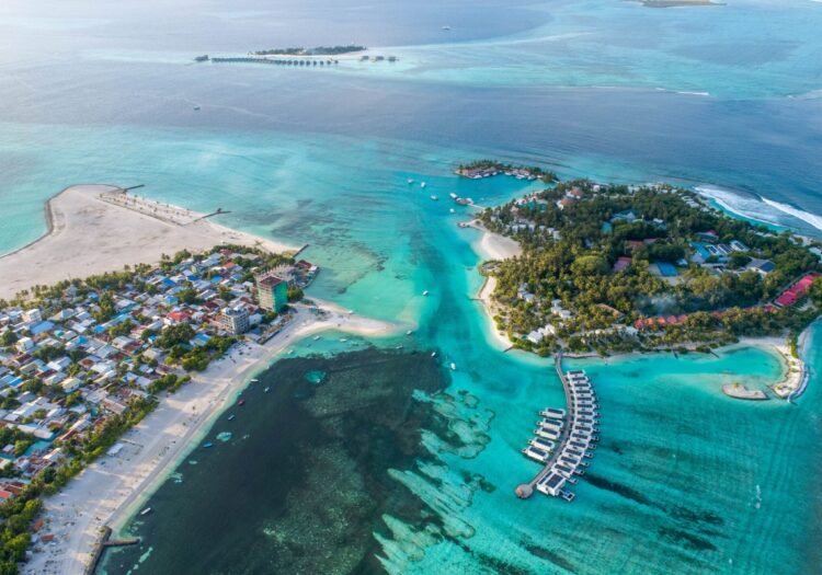 An aerial view of a tropical island with clear turquoise waters and overwater bungalows in the Maldives