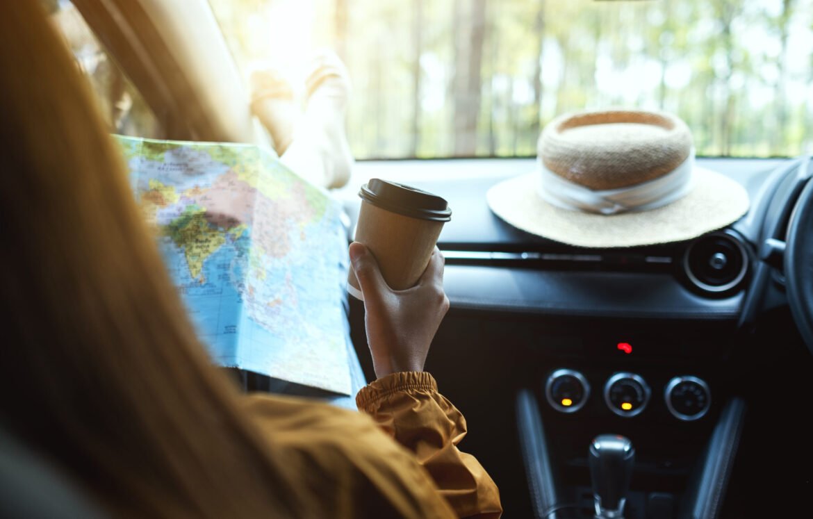 Closeup image of a woman reading a map for direction and drinkin Closeup image of a woman reading a map for direction and drinking coffee in the car