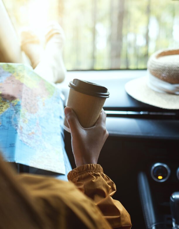Closeup image of a woman reading a map for direction and drinking coffee in the car