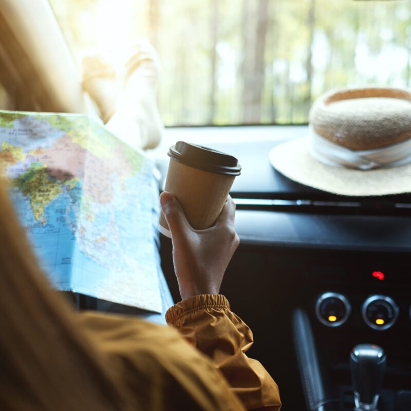 Closeup image of a woman reading a map for direction and drinking coffee in the car
