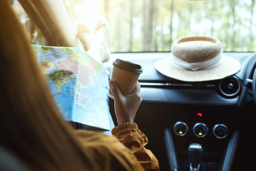 Closeup image of a woman reading a map for direction and drinking coffee in the car