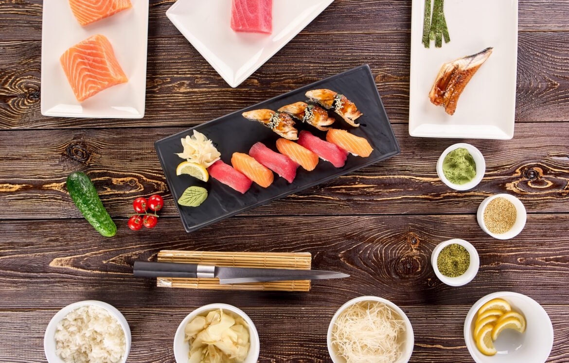 Concept of many plates of sushi and bowls of side dish. Concept of many plates of sushi and bowls of side dish. Cooking concept, nigiri sushi on kitchen and spices on wooden table, top view.
