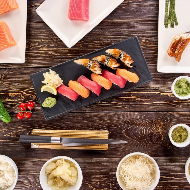 Concept of many plates of sushi and bowls of side dish. Cooking concept, nigiri sushi on kitchen and spices on wooden table, top view.