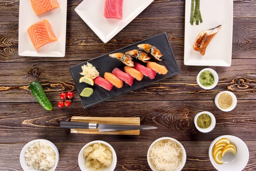 Concept of many plates of sushi and bowls of side dish. Cooking concept, nigiri sushi on kitchen and spices on wooden table, top view.