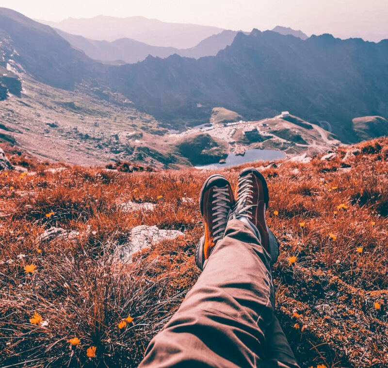 Legs of traveler sitting on a high mountain top in travel. Freedom concept