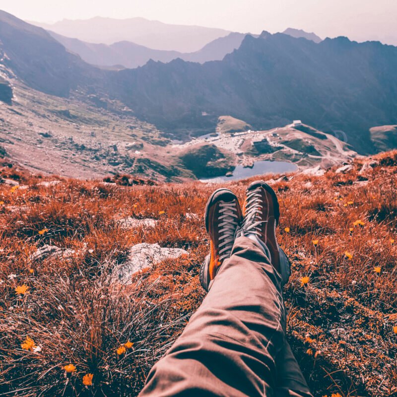 Legs of traveler sitting on a high mountain top in travel. Freedom concept