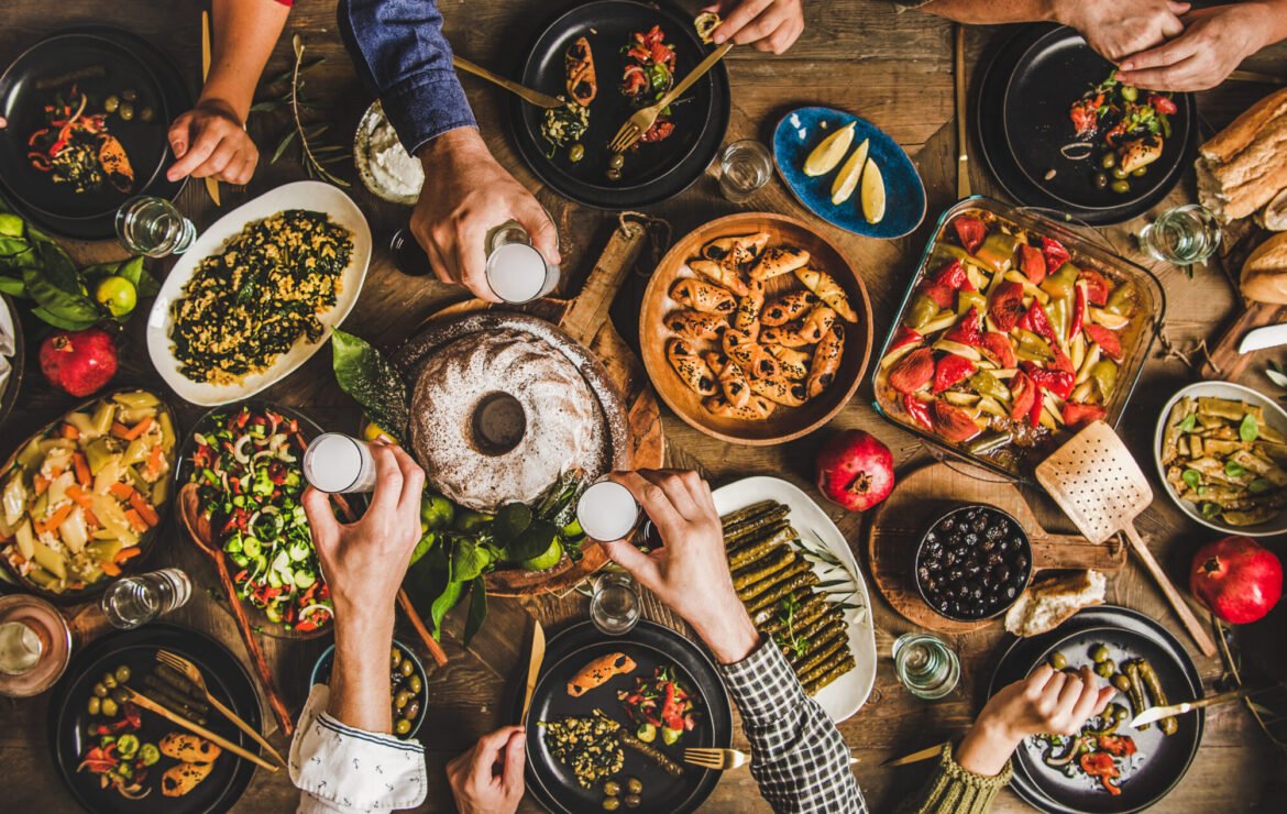 Traditional Turkish celebration dinner with food and raki, wide composition Traditional Turkish celebration dinner. Flat-lay of people eating Turkish salads, cooked vegetables, meze starters, pastries and drinking raki drink, top view, wide composition. Middle Eastern cuisine