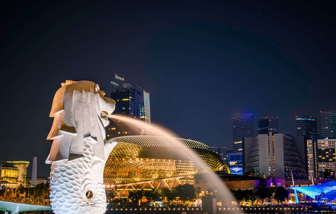 Merlion statue fountain in Merlion Park and Singapore city skyline at night.