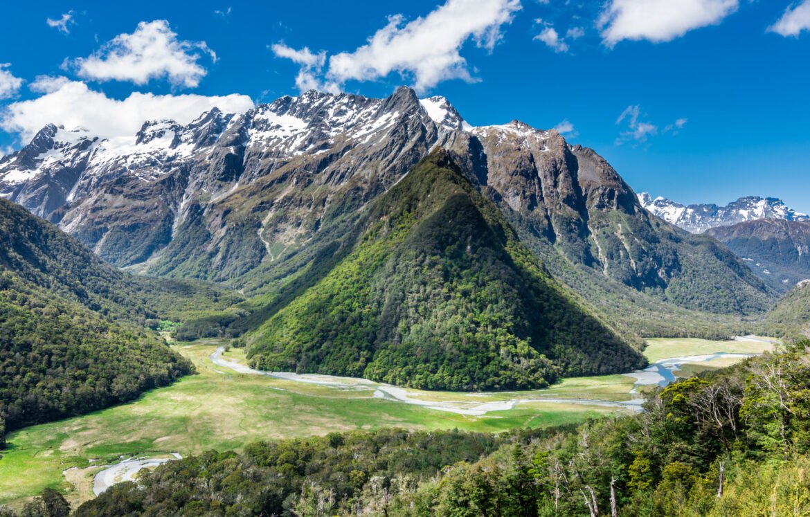 Panoramic view of the Humboldt Mountains in New Zealand, featuring lush green valleys, snow-capped peaks, and winding rivers under a vibrant blue sky.