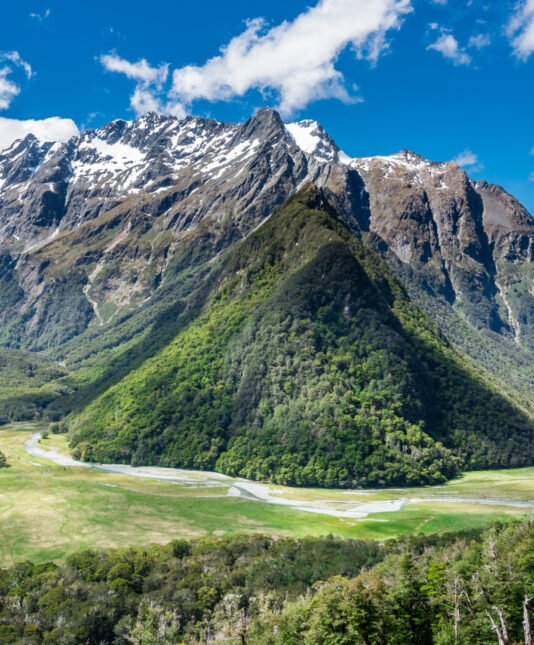 Panoramic view of the Humboldt Mountains in New Zealand, featuring lush green valleys, snow-capped peaks, and winding rivers under a vibrant blue sky.