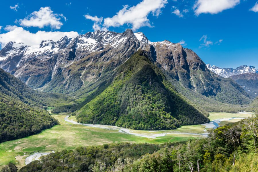 Panoramic view of the Humboldt Mountains in New Zealand, featuring lush green valleys, snow-capped peaks, and winding rivers under a vibrant blue sky.